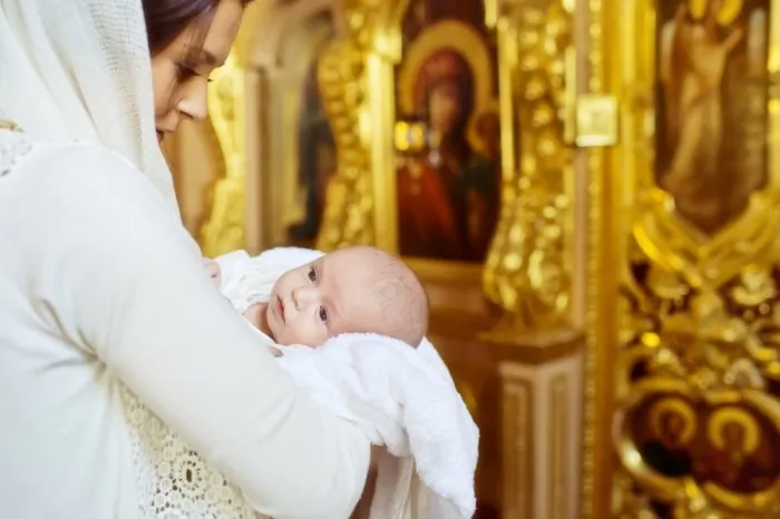 Крестные родители с покрытой головой и руками, покрытыми кителем, проводят церемонию крещения