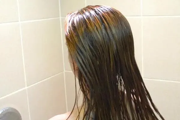 Девушка наносит масло на волосы