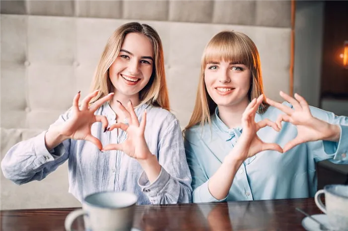 Две девушки в кафе показывают свои сердца руками.