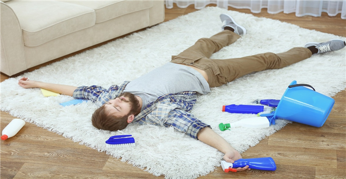 Мужчина лежит на ковре с моющими средствами и ведром.